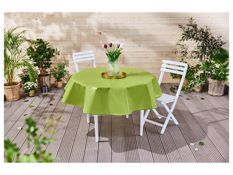 Ein grüner Tischdecke auf einem runden Tisch mit zwei weißen Stühlen auf einer Terrasse.