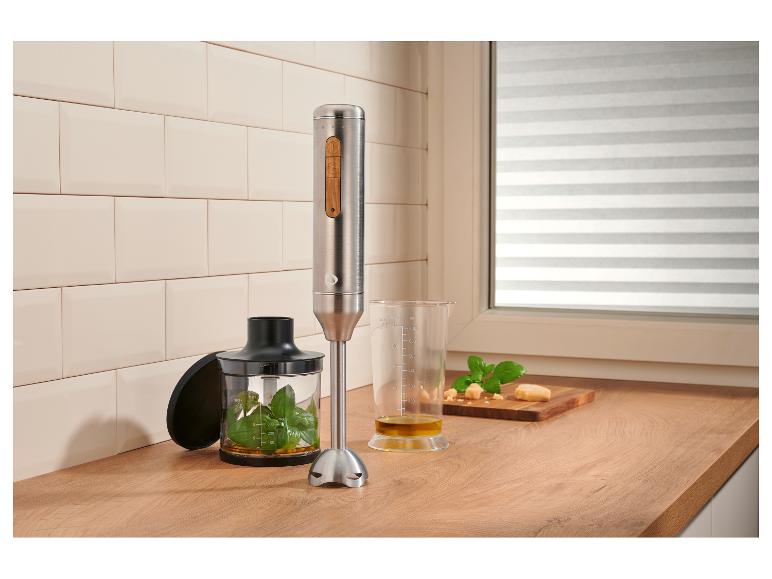 Edelstahl-Stabmixer mit Holz-Akzenten, der Pesto auf einer Holzarbeitsplatte zubereitet.