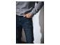 Mann trägt ein graues Sweatshirt und dunkelblaue Jeans, mit einer Hand in der Tasche.
