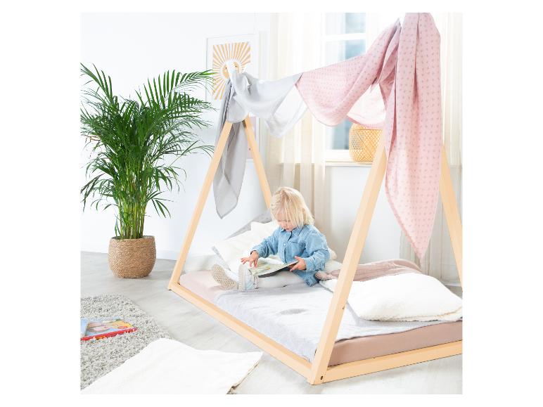 Ein Kind liest ein Buch in einem Montessori-Holzbett, dekoriert mit rosa und grauen Stoffen.