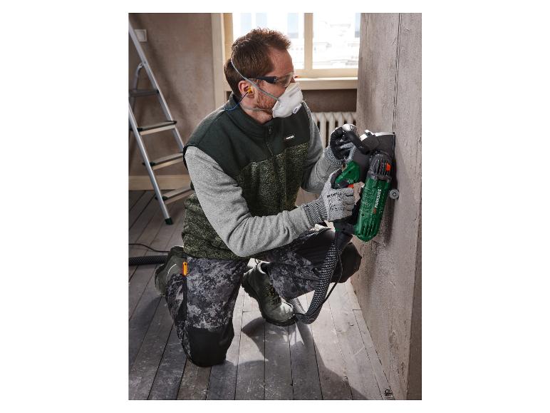 Ein Mann verwendet eine Parkside Schleifmaschine, um eine Wand zu bearbeiten.