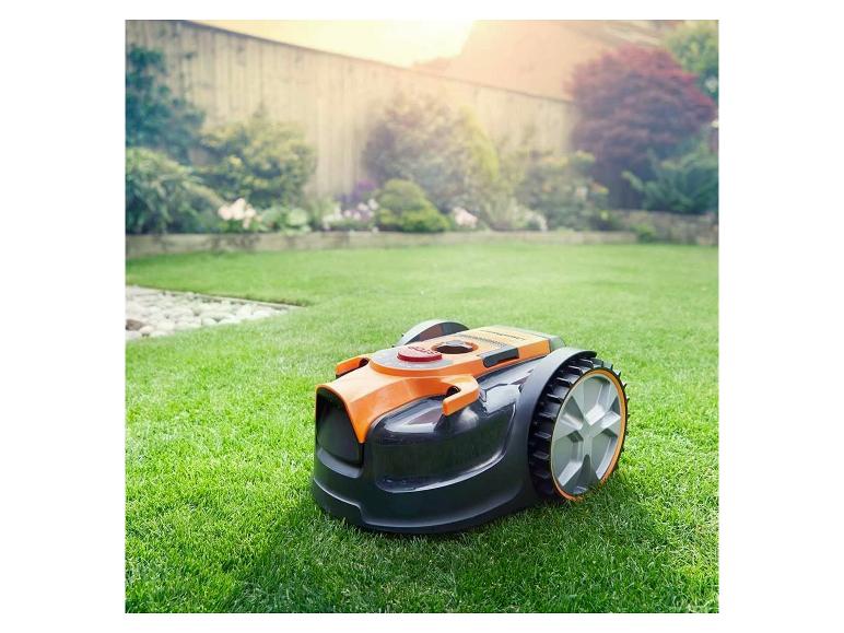 Orange-schwarzer Mähroboter auf grünem Rasen in einem sonnigen Garten.