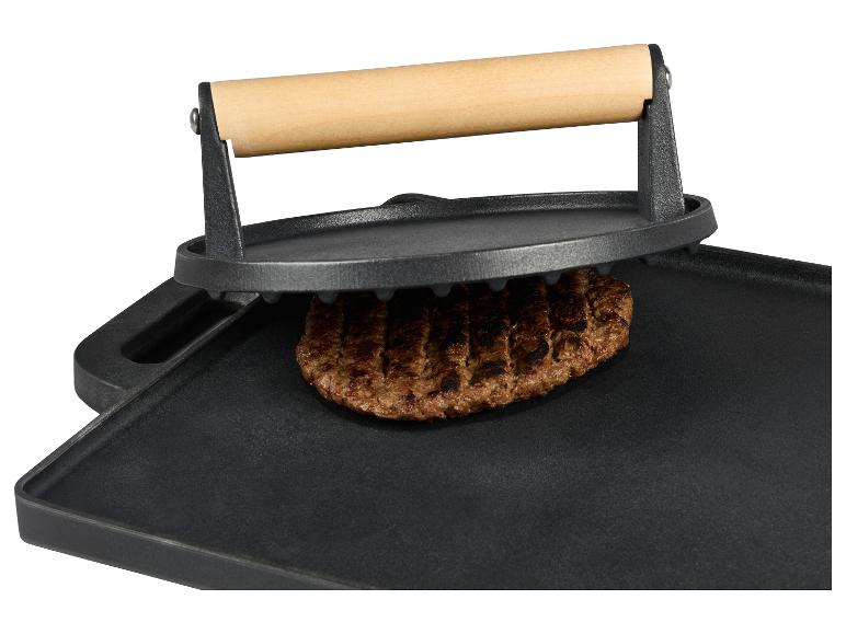 Gusseisen-Grill mit Burger und Presse auf weißem Hintergrund.