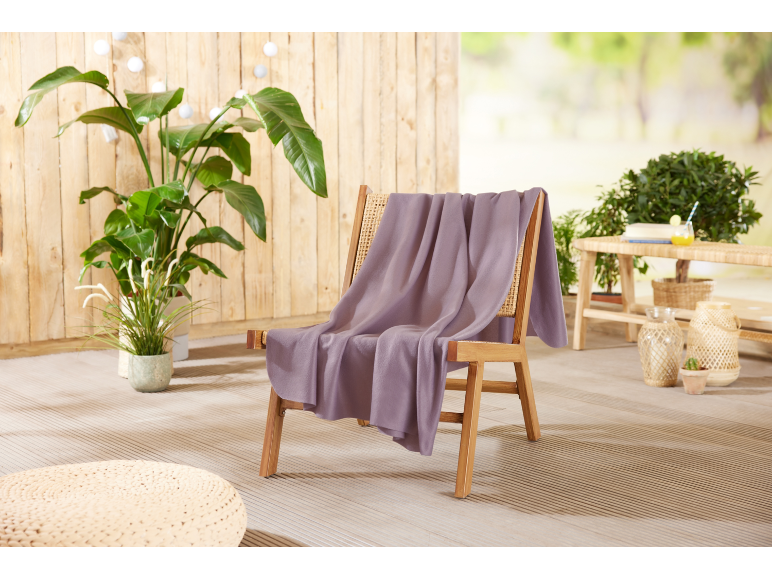 Lila Decke auf einem Holzstuhl auf einer Terrasse mit Pflanzen und Dekoration.