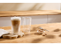 Zwei Latte Macchiato Gläser, eines voll und eines leer, mit Keksen und einem Löffel.