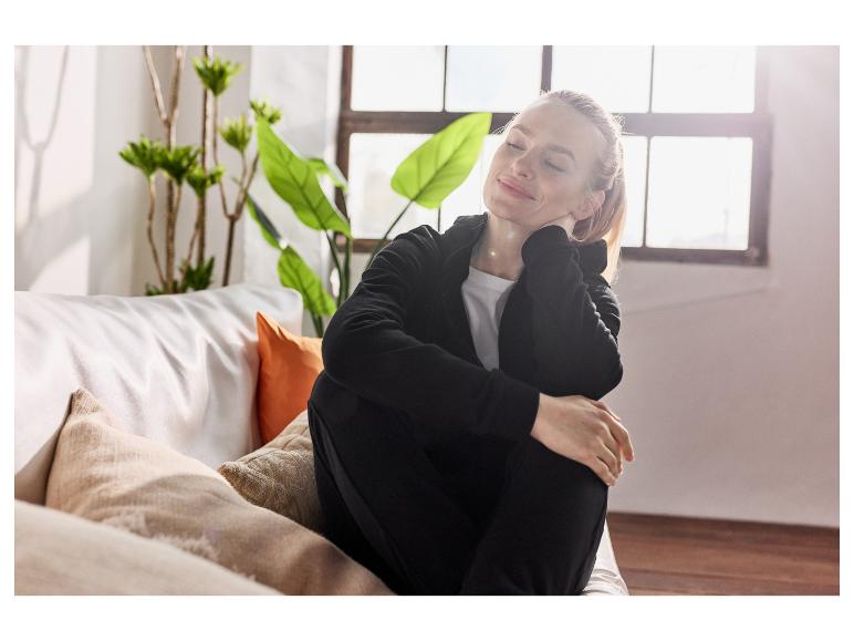 Eine Frau entspannt sich in einem schwarzen Trainingsanzug auf der Couch.