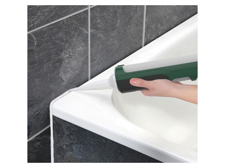 Hand trägt Dichtmittel auf den Rand einer weißen Badewanne vor dunkelgrauen Fliesen auf