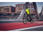 Mann in gelber Fahrradjacke und schwarzem Helm auf einem E-Bike auf einer Brücke.