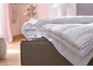Gefaltete weiße Bettdecke mit blauem Rand auf einem Bett in einem Schlafzimmer mit rosa Wänden.