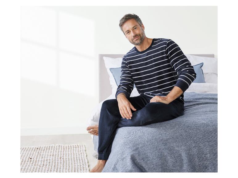 Mann in gestreiftem Pyjama, der auf einem Bett sitzt.