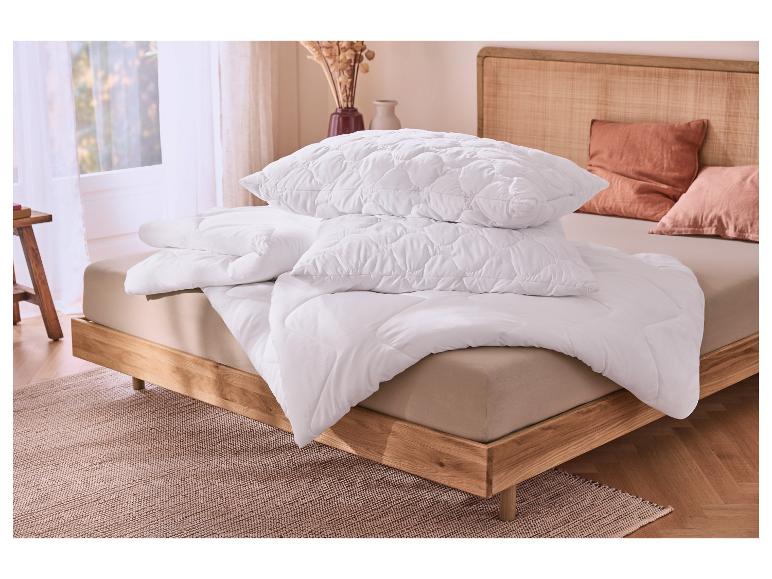 Bett mit weißer Bettdecke und Kissen in einem hellen Schlafzimmer mit Holzkopfteil.