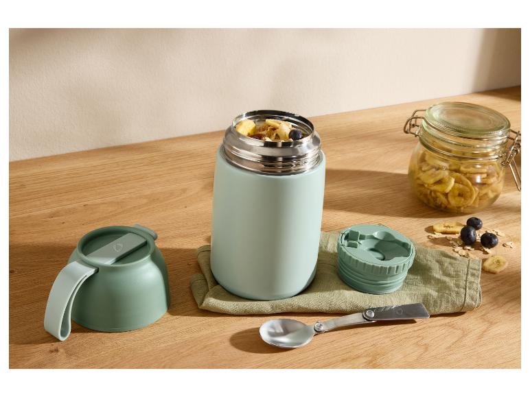 Essens-Thermoskanne mit Frühstück, Schale, Löffel und Glas getrockneter Bananen auf Holztisch.