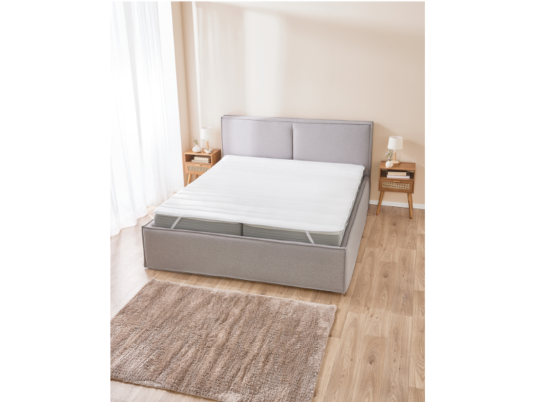Graues Boxspringbett mit weißem Topper in einem Schlafzimmer mit Holzboden und Teppich.