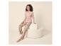 Frau in rosa Pyjama mit Blumenmuster und „Stay Cozy“-Aufschrift auf einem cremefarbenen Pouf.