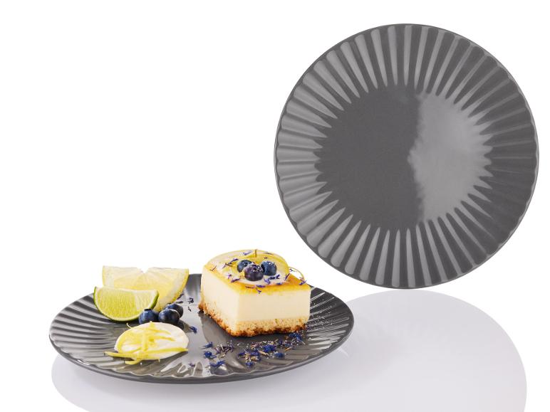 Ein grauer Teller mit einem Stück Zitronen-Cheesecake und Limettenspalten.