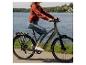 Frau fährt E-Bike an einem See an einem sonnigen Tag.