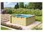 Quadratischer Holzpool mit blauem Wasser in einem Garten mit Büschen und Palettensofa.