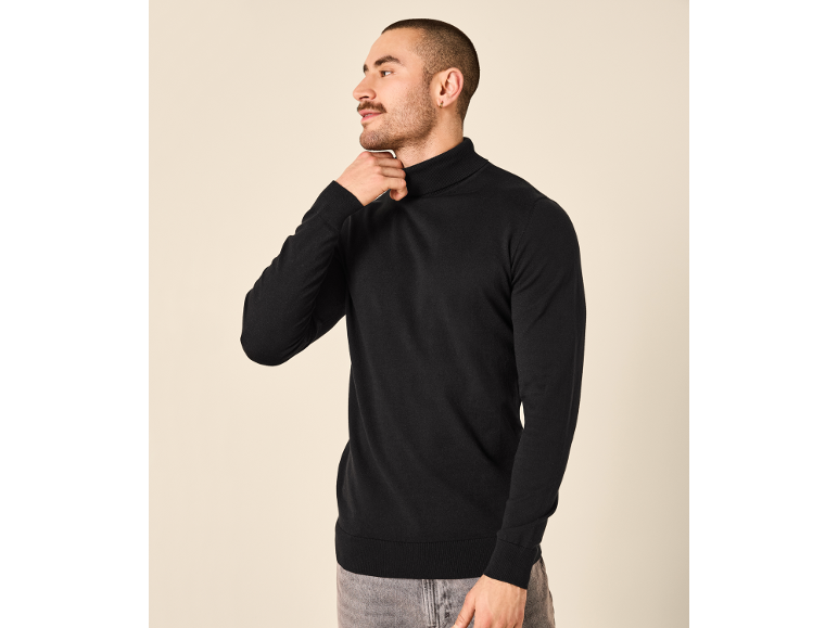 Mann in einem schwarzen Rollkragenpullover und einer grauen Hose.