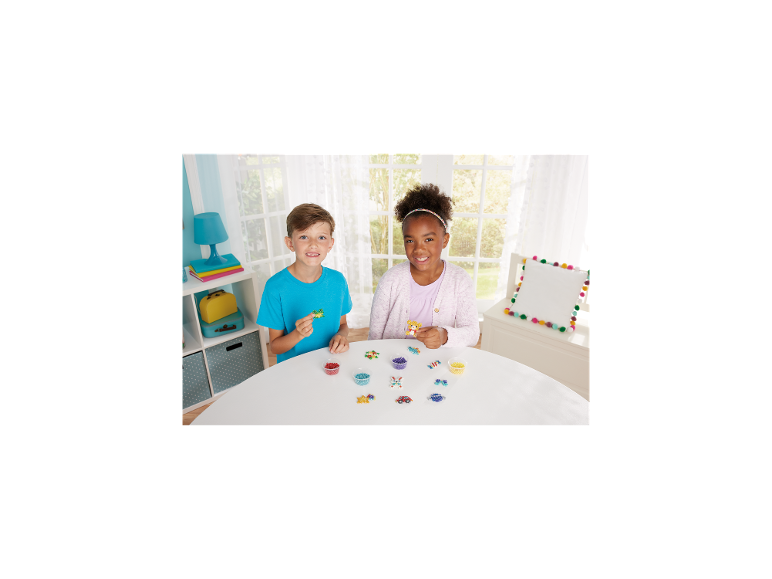 Zwei Kinder spielen mit Bügelperlen und kreieren bunte Formen auf einem weißen Tisch.