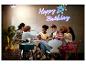 Freundesgruppe feiert Geburtstag mit einem Projektor, der „Happy Birthday“ an die Wand projiziert.