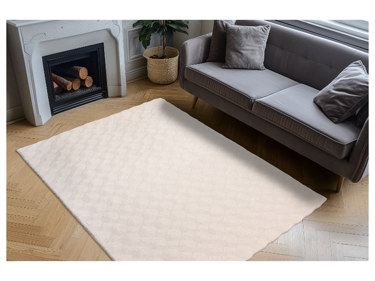 Cremefarbener Teppich mit Textur auf hellem Holzboden vor einem grauen Sofa.