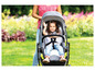 Ein Kind in einem grauen Kinderwagen in einem grünen Garten.