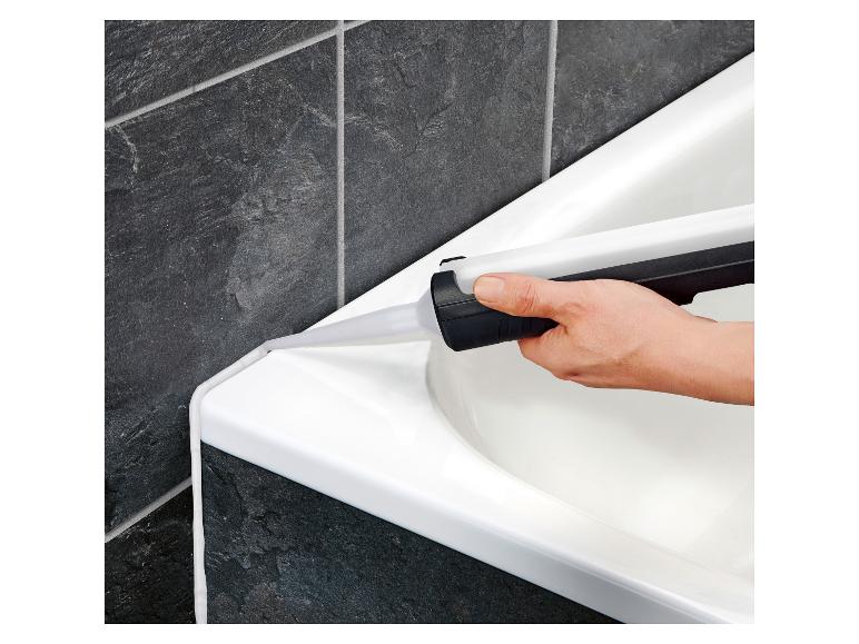 Eine Hand trägt weißen Dichtstoff auf den Wannenrand neben dunklen Fliesen auf.