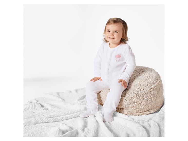 Ein Baby sitzt auf einem Plüschkissen und trägt einen weißen Strampler mit einem Wolkenmuster.