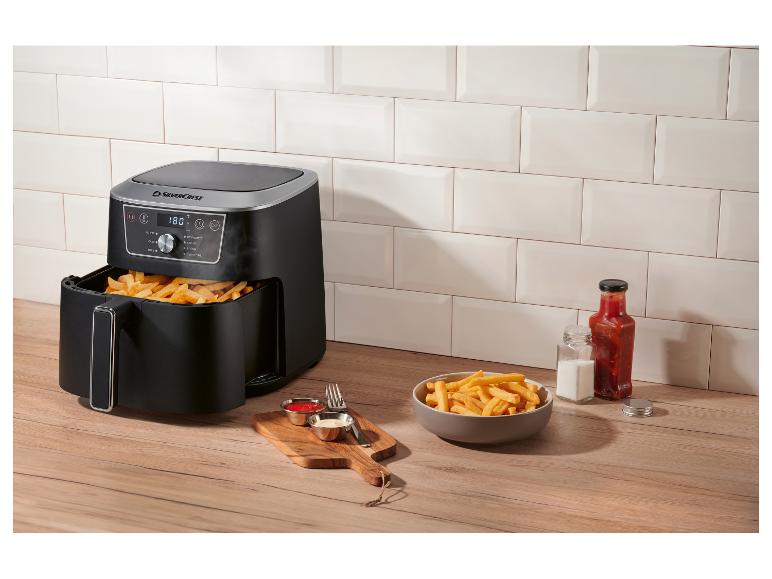 Heißluftfritteuse mit Pommes Frites, Ketchup und Mayonnaise auf einer Holztheke.