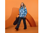 Eine Frau in einer blau gemusterten Skijacke und einer schwarzen Hose hält ein Snowboard.