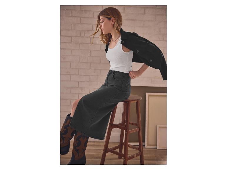 Frau in weißem Top und schwarzem Jeansrock sitzt auf einem Holzhocker.