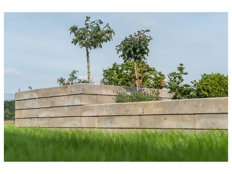 Erhöhte Betonbeete mit Pflanzen und Sträuchern, grüner Rasen im Vordergrund.