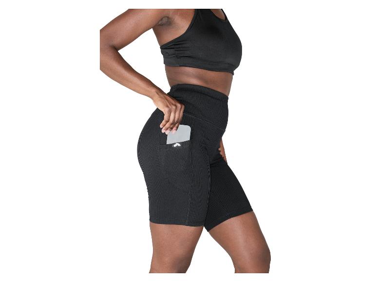 Frau in schwarzem geripptem Sport-BH und Radlerhose mit Handy in der Seitentasche.