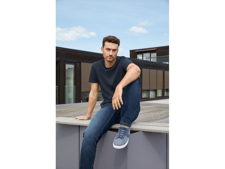 Mann in einem T-Shirt und blauen Jeans, der auf einem Dach sitzt.