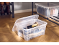 Transparente Aufbewahrungsboxen mit Schuhpflegeprodukten und Schuhen auf einem Regal.