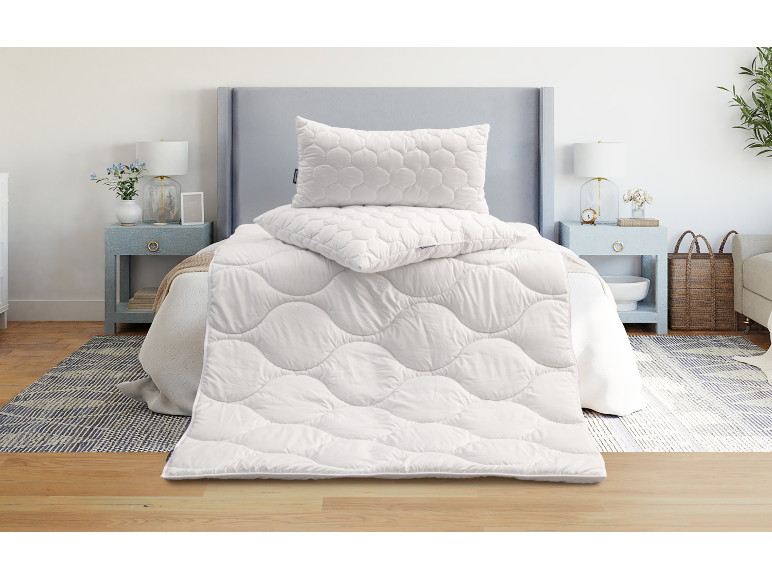 Weiße gesteppte Decke und Kissen auf einem Bett im Schlafzimmer.