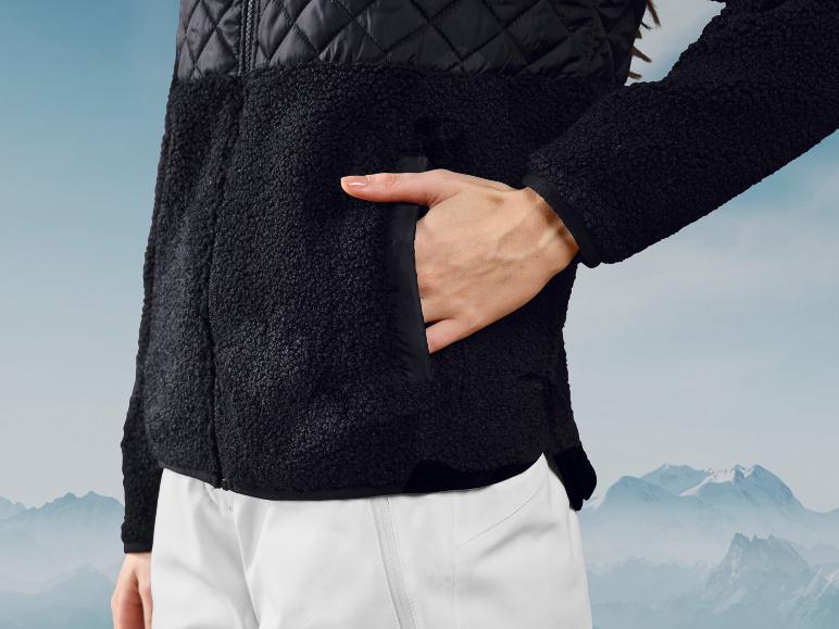 Schwarze Fleecejacke und weiße Hose vor einem Bergpanorama.