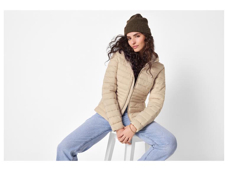 Frau in beiger Steppjacke, hellblauer Jeans und olivgrüner Mütze