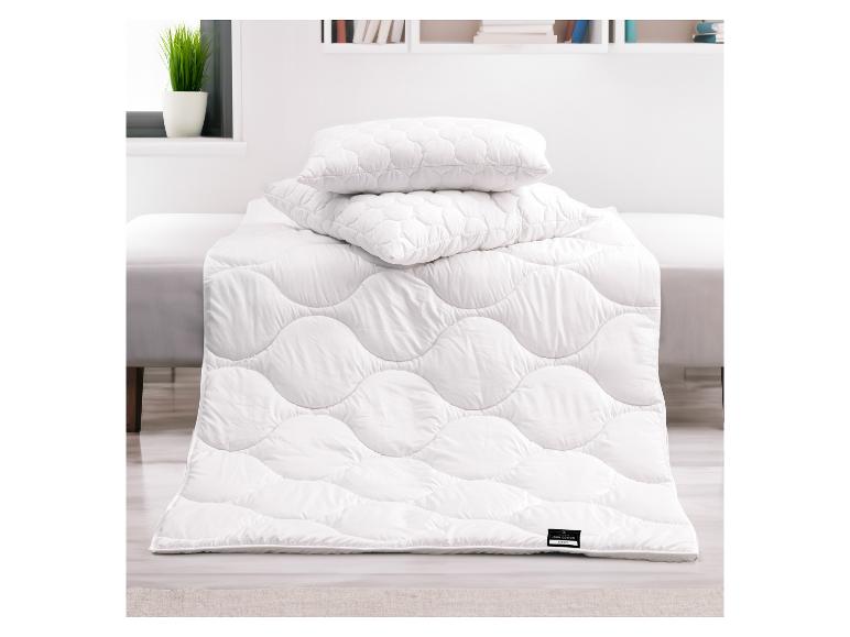 Weiße Bettdecke und Kissen mit Wellenmuster auf einem Bett in einem hellen Raum.