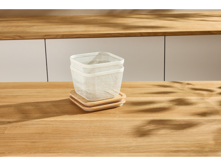 Zwei weiße Drahtkörbe mit Holzdeckeln auf einem Holztisch.