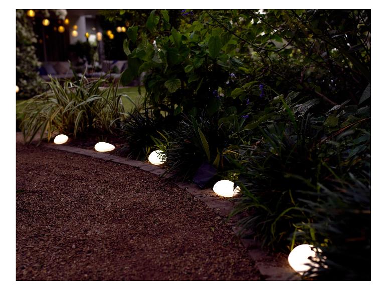 Solarleuchten in Steinoptik beleuchten einen Gartenweg.