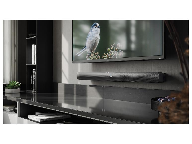 Fernseher mit Soundbar in einem modernen Wohnzimmer, mit Büchern und Pflanze.