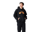 Lächelnder Mann in schwarzem Hoodie mit orangefarbenem Muster und schwarzer Jogginghose.