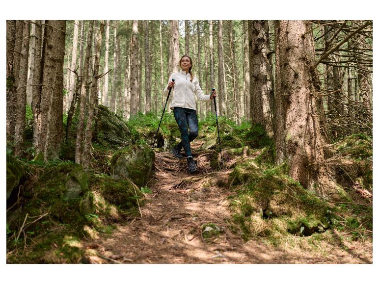 Frau in Jacke und Leggings, wandert mit Trekkingstöcken im Wald.