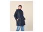 Frau in marineblauer Regenjacke und Jeans, lächelnd mit Händen in den Taschen.