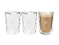 Drei doppelwandige Gläser, eines davon gefüllt mit einem Kaffeegetränk mit Milchschaum.