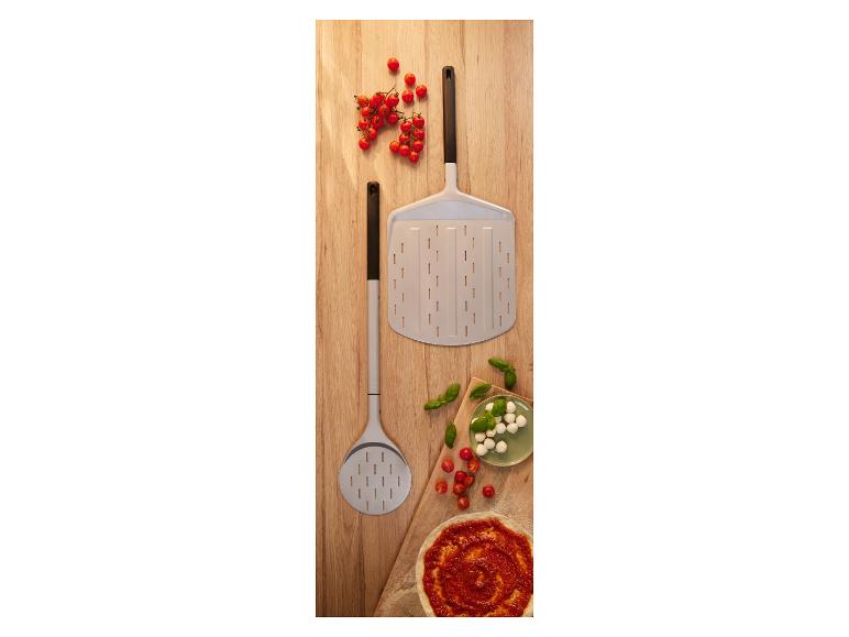 Pizzaschieber mit Kirschtomaten, Mozzarella, Basilikum und Pizzaboden auf einem Holzbrett.