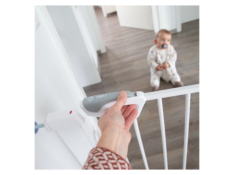 Hand öffnet ein weißes Schutzgitter mit Baby im Hintergrund