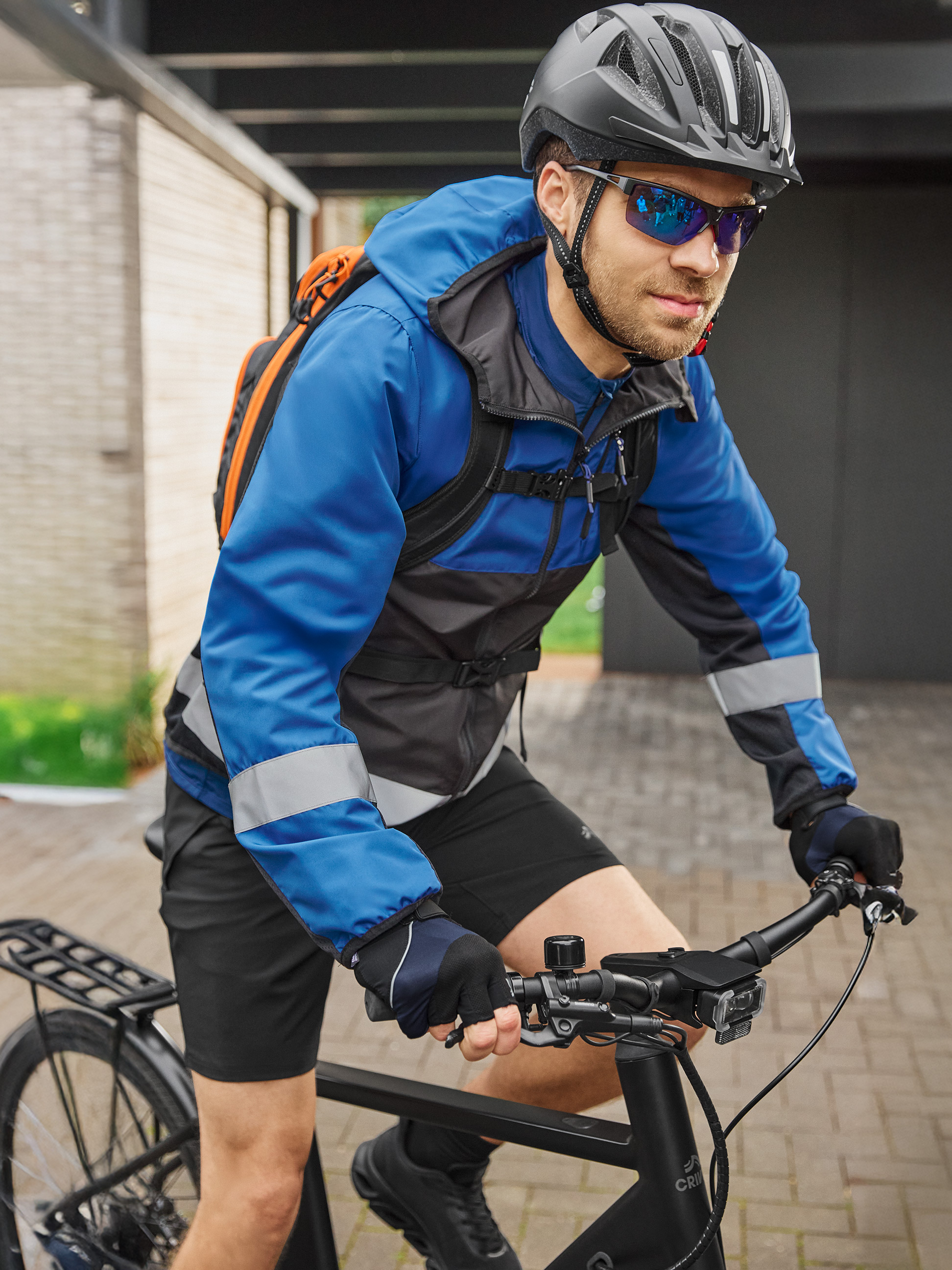 Radfahrer in blau-schwarzer Radjacke, Helm und Sonnenbrille, auf einem schwarzen Fahrrad.
