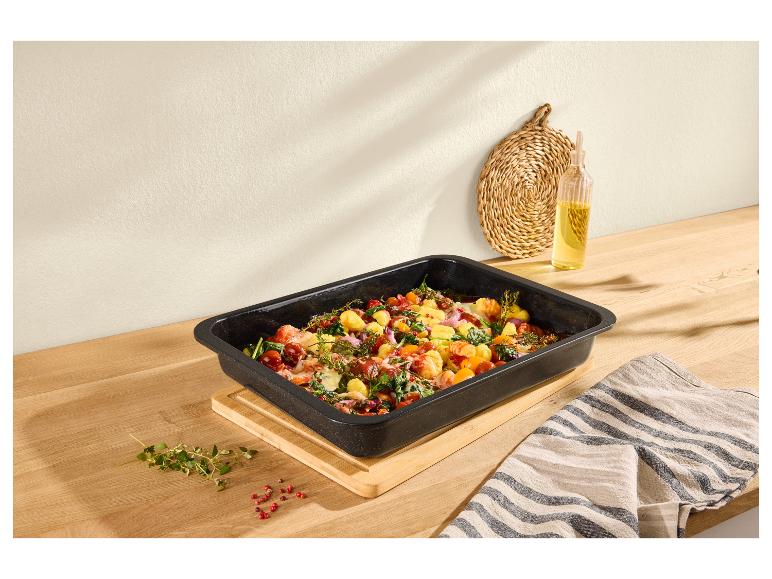 Auflaufform gefüllt mit Gnocchi, Tomaten, Spinat und Kräutern auf einem Holztisch.